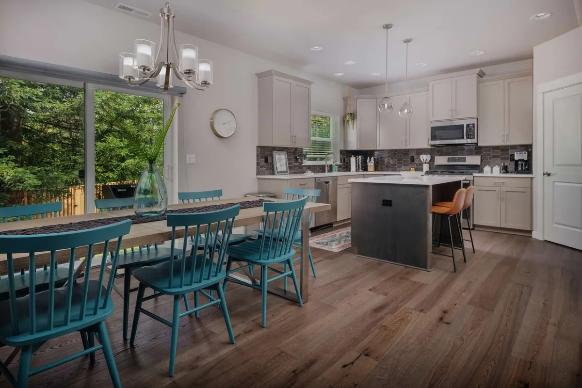This image highlights a spacious dining table positioned beneath a stylish light fixture. The kitchen island is visible nearby, and large windows offer views to the outdoors, suggesting a bright, communal atmosphere ideal for shared meals or casual gatherings. The setting feels adaptable for both family time and catching up with friends after a productive workday.
