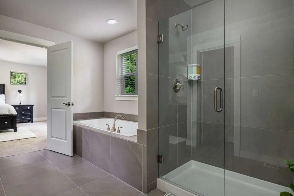 A luxurious bathroom with a freestanding bathtub, glass-enclosed walk-in shower, and a large window allowing natural light to flood the space. Modern fixtures and a tranquil vibe suggest spa-like relaxation.