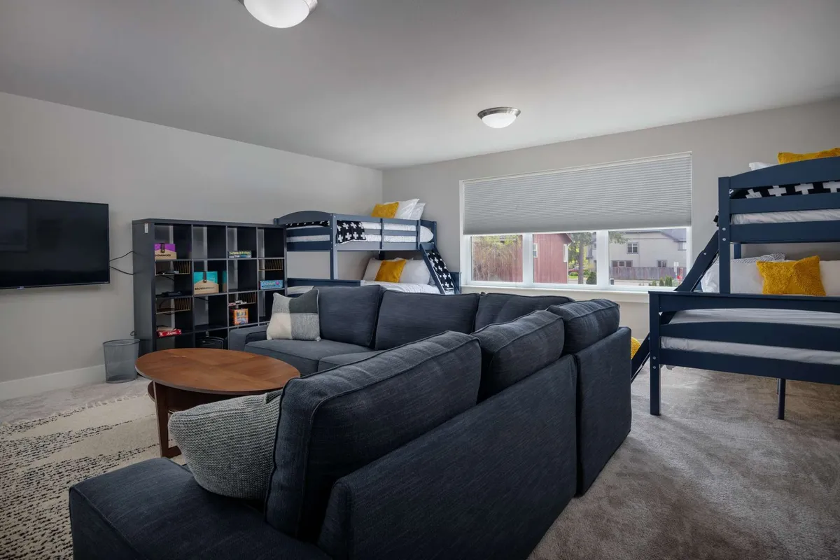 A playful bunk/media room featuring bunk beds, a comfy sofa, a TV, and a coffee table. The room is set up for both relaxation and entertainment, ideal for kids and teens to socialize and enjoy movie nights.