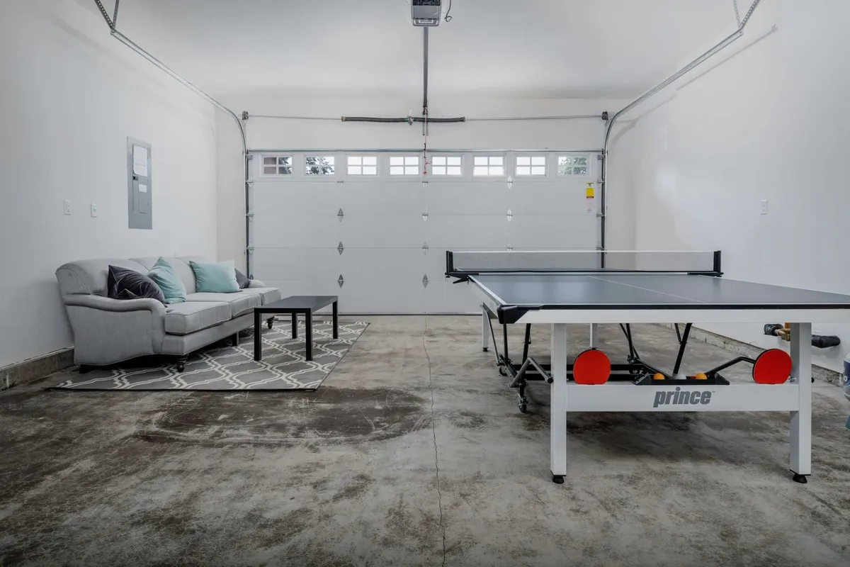 A lively recreation room set in a converted garage, featuring a ping pong table, comfortable seating, and a visible garage door. The scene exudes a playful and relaxed mood, suggesting hours of friendly competition and group fun.