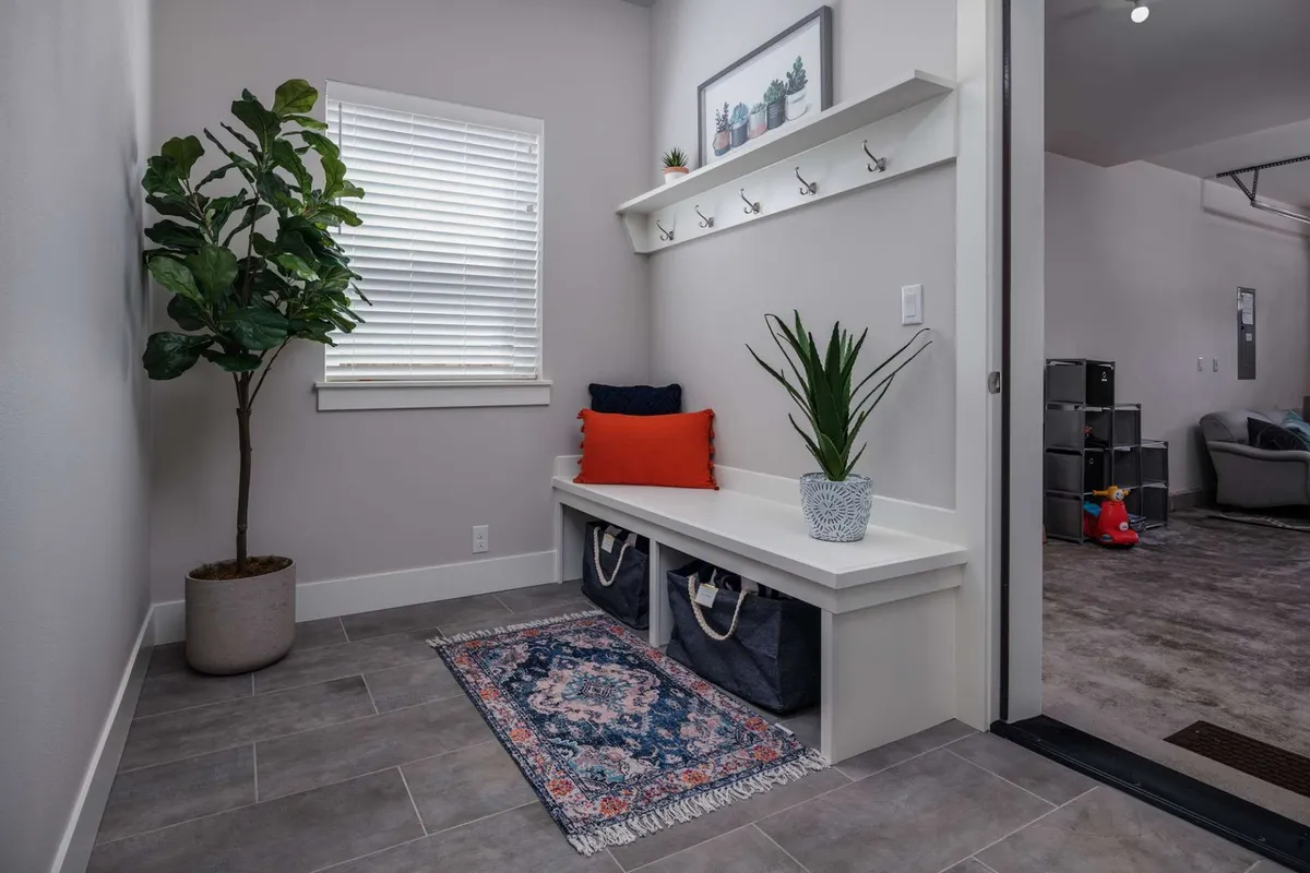 A tidy, inviting entryway featuring a potted plant, cushioned bench, wall hooks for leashes or bags, and a decorative shelf. The space feels organized and welcoming, offering a functional spot for families and their pets to prepare for outdoor adventures.